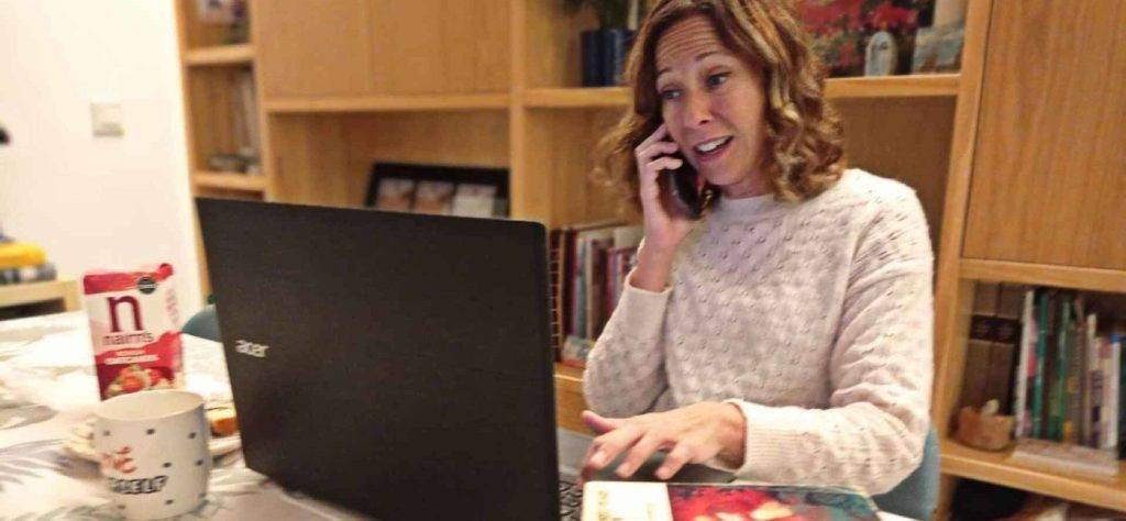 mujer que quiere estudiar inglés en Inglaterra y trabajar, hablando con su móvil, tecleando en su portátil