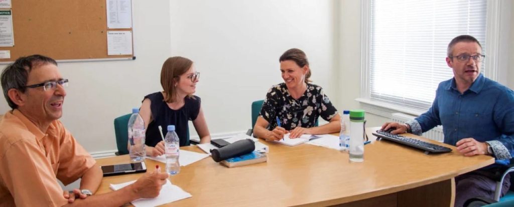 Estudiantes de inglés mayores Brighton 40+ sentados alrededor de una mesa con su profesor