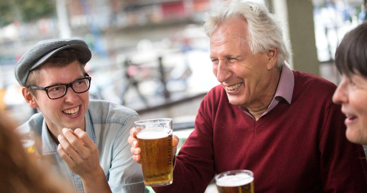 tres adultos riéndose mientras beben una pinta de cerveza