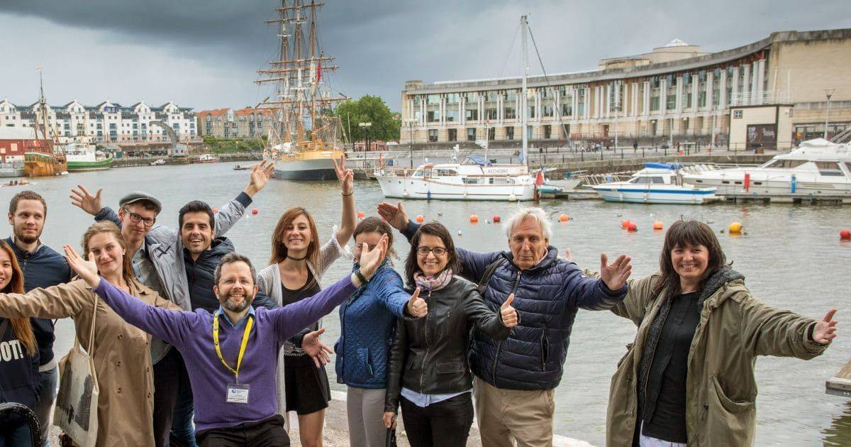 foto grupal de estudiantes de inglés adultos y su profesor sonriendo con el puerto de Bristol al fondo