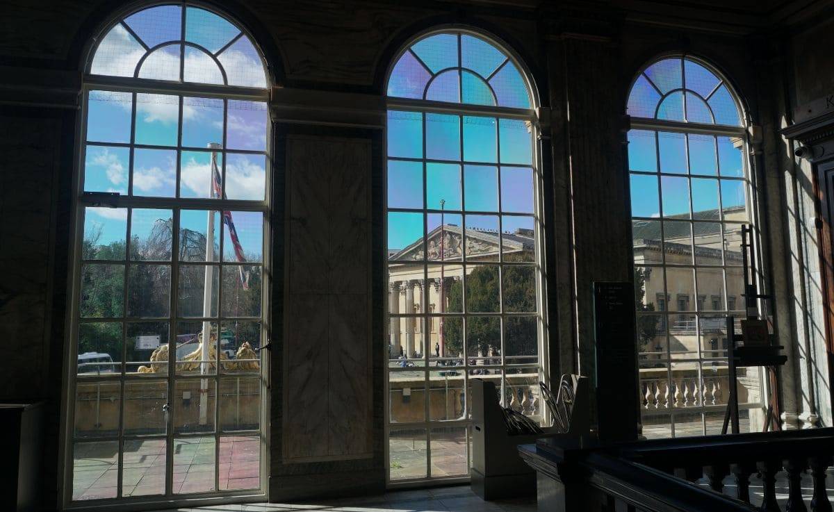 Una vista de un día soleado a través de 3 grandes ventanas arqueadas de una galería de arte