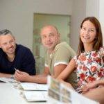 Tres adultos mayores de 30 años sonriendo en una clase de inglés