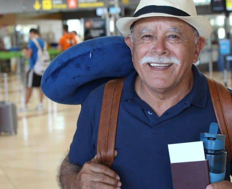 hombre mayor sonriendo en el aeropuerto con rucsac y sombrero y pasaporte en mano