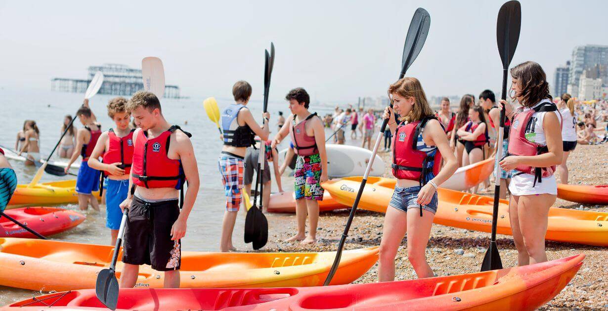 adolescentes preparándose para hacer kayak en la playa de Brighton