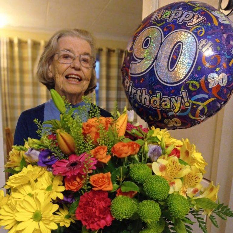 mujer de 90 años celebrando su cumpleaños con flores y un globo