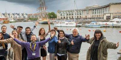 foto grupal de estudiantes de inglés adultos y su profesor sonriendo con el puerto de Bristol al fondo